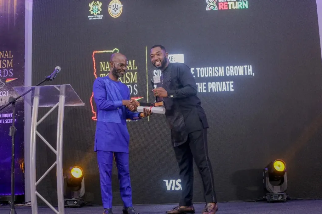 Handshake on stage at a Ghana Tourism Authority ceremony, with a National Tourism Awards 2021 digital backdrop