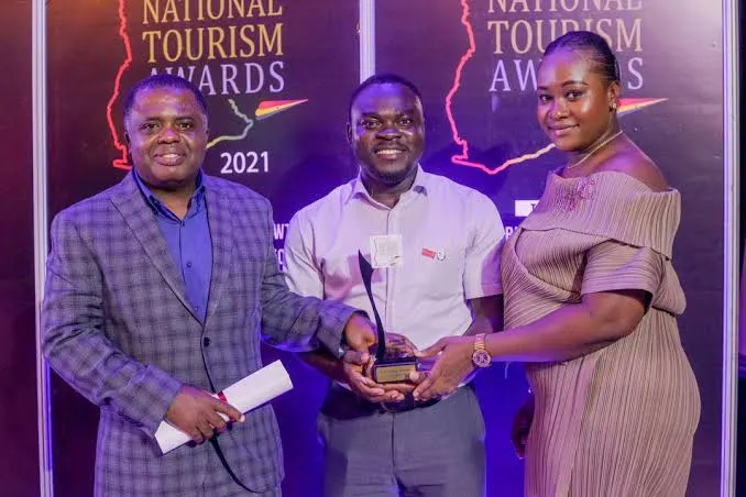 Three people holding a trophy and a rolled certificate in front of a National Tourism Awards 2021 backdrop