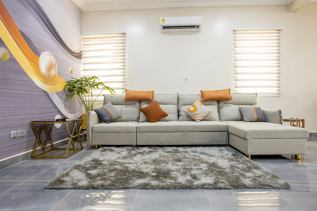 Waiting lounge at Plantsville in Dansoman, Accra, with a grey sofa, orange cushions, a potted plant, and a mural wall